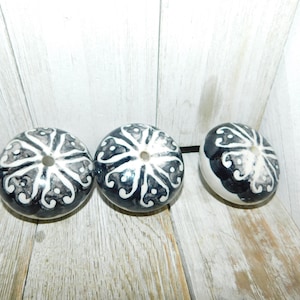 May include: Three round ceramic beads with a black and white floral design. The beads have a hole in the center for stringing.
