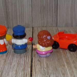 May include: A set of four plastic figurines, including a chef, a police officer, a girl, and a red toy car. The figurines are all facing away from the camera.