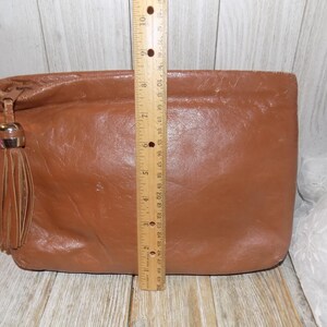 May include: A brown leather clutch with a tassel. The clutch is about 7 inches tall.