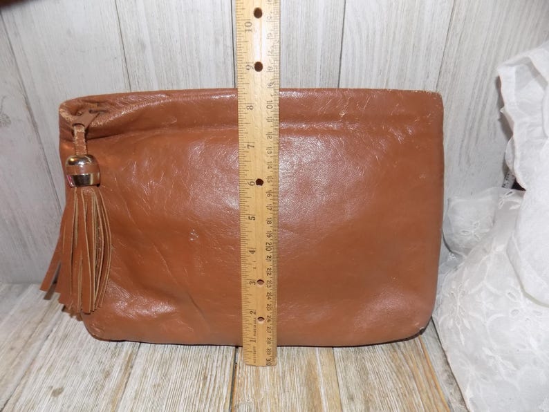May include: A brown leather clutch with a tassel. The clutch is about 7 inches tall.