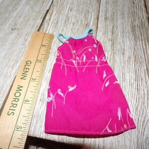 May include: A pink sleeveless dress with a floral print and a light blue trim around the neckline. The dress is approximately 5 inches long.