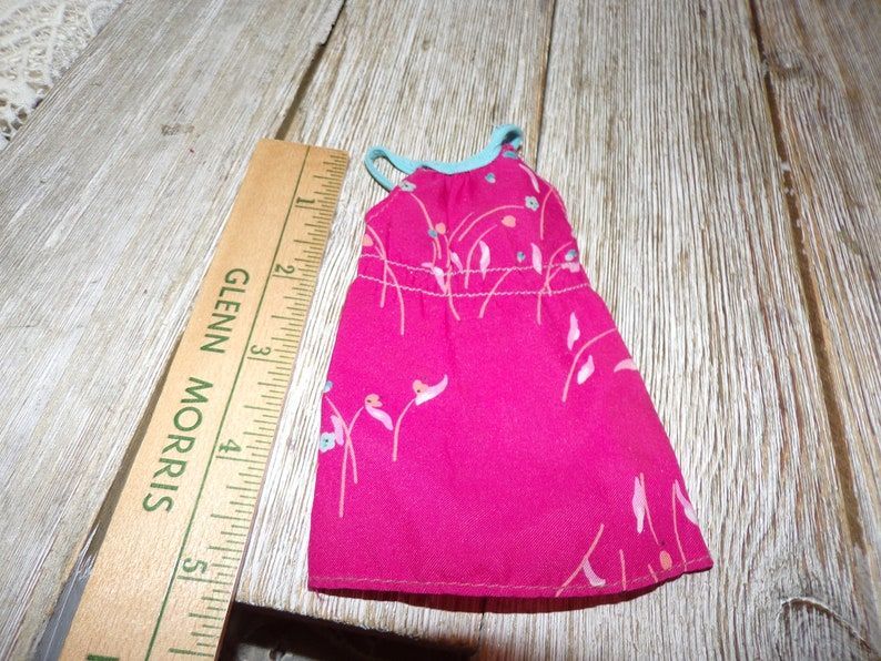 May include: A pink sleeveless dress with a floral print and a light blue trim around the neckline. The dress is approximately 5 inches long.