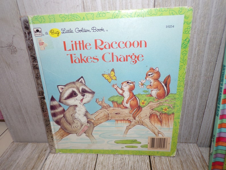 May include: A Little Golden Book titled "Little Raccoon Takes Charge". The cover features a raccoon sitting on a branch over a stream, with two chipmunks and a butterfly nearby. The book is blue with a green border.