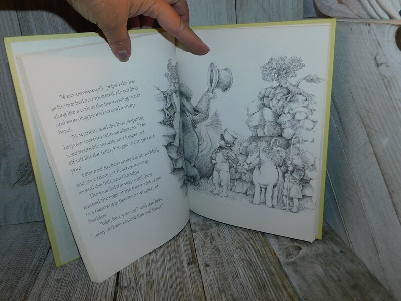 May include: A black and white illustration from a children's book showing a bear, a fox, two children, and a donkey. The bear is standing on a pile of rocks and is talking to the fox. The fox is swimming in a river. The children and the donkey are walking towards the bear. The text in the image reads: "Waaoooowwww!! yelped the fox as he thrashed and spunered. He bobbed along like a cork in the fast moving water and soon disappeared around a sharp bend."
