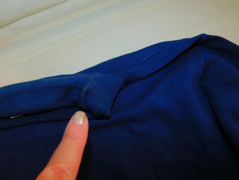 May include: Close-up of a dark blue fabric with a fold in the fabric. The fabric is smooth and has a slight sheen.