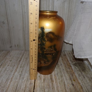 May include: A gold ceramic vase with a painted scene of a Japanese mountain landscape. The vase is approximately 9 inches tall.