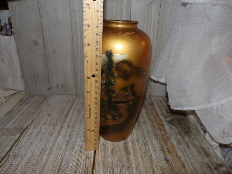 May include: A gold ceramic vase with a painted scene of a Japanese mountain landscape. The vase is approximately 9 inches tall.