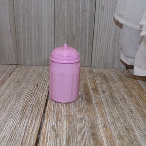 May include: A pink plastic baby bottle with a lid. The bottle has a textured design.
