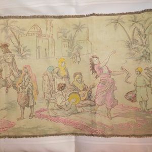 May include: A vintage tapestry depicting a scene of people in a Middle Eastern marketplace. The tapestry features a woman dancing, men playing music, and a donkey. The tapestry is woven with colorful threads and has a fringed border.