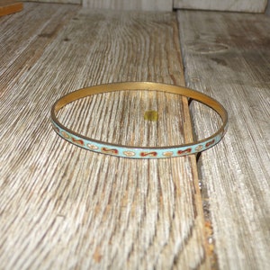 May include: A gold bangle bracelet with a blue and red enamel design. The design features a repeating pattern of swirls and dots.