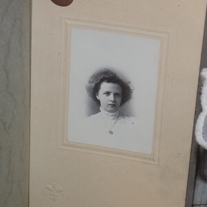 May include: A vintage black and white portrait of a woman in a white dress and necklace. The photograph is in a decorative frame, set against a neutral background. The woman has curly hair and is looking at the camera.
