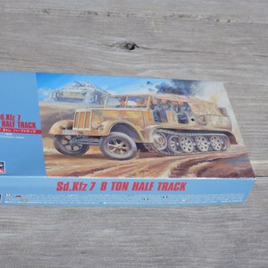 May include: A model kit box for the Sd.Kfz 7 8 Ton Half Track. The box features an illustration of the vehicle in a desert setting. The text on the box includes "Sd.Kfz 7 8 TON HALF TRACK" and "1:72". The box is blue.