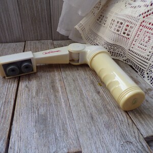 May include: A white plastic body massager with two round heads and a swivel joint. The massager has the words "Body Massager" printed on it in red.