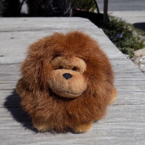 May include: A brown plush monkey toy with a long, shaggy coat. The monkey has a black nose and black eyes.