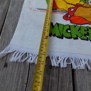 Peut inclure: Serviette en coton blanc avec un motif Mickey Mouse color&eacute; et le texte "MICKEY MOUSE". La serviette a une bordure &agrave; franges et mesure environ 104 cm de long.