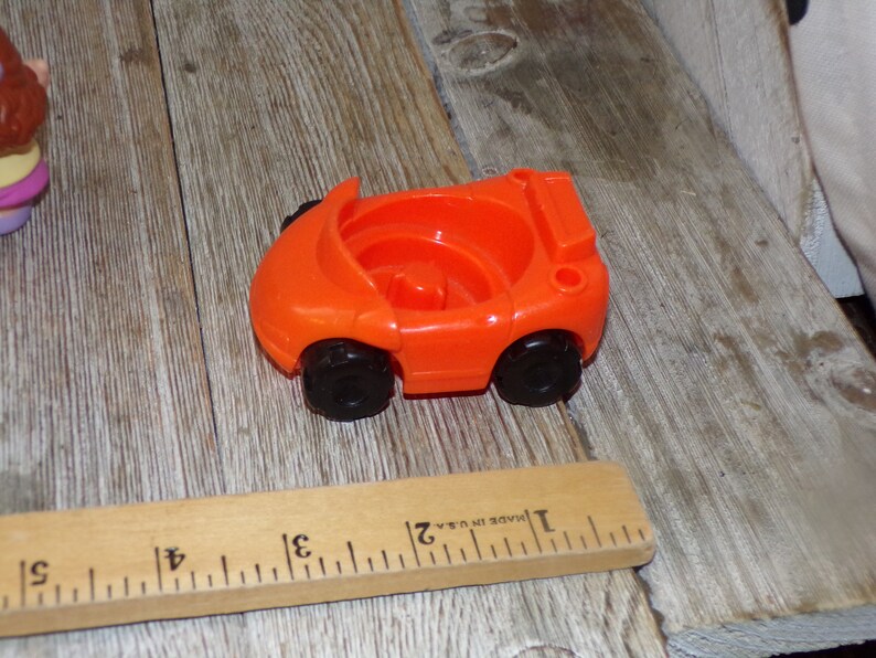 May include: Orange plastic toy car with black wheels. The car is approximately 5 cm long.