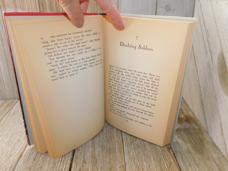 May include: A close-up of two pages from a vintage book titled "The Shadow of Robbers' Roost" and "Doubting Soldiers". The pages are yellowed with age and the text is printed in black ink.