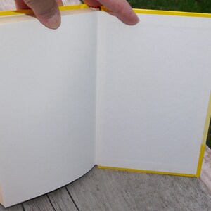 May include: A yellow hardback book with white pages is open to reveal a blank page.