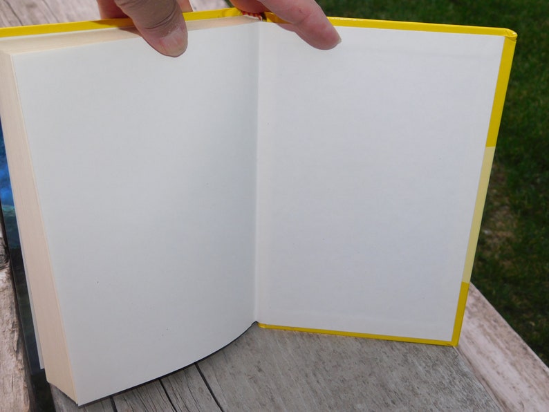 May include: A yellow hardback book with white pages is open to reveal a blank page.