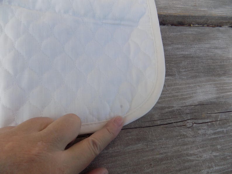 Op de afbeelding: Witte quilted stof met een witte binding rond de rand. De stof heeft een ruitpatroon.