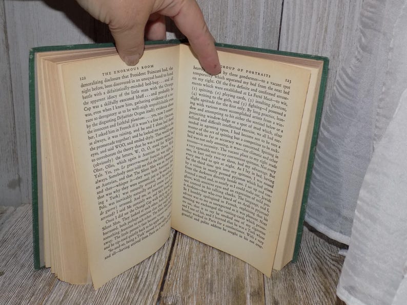 May include: An open book with green covers and white pages. The text on the pages is in black and discusses the "Enormous Room" and a "Group of Portraits".