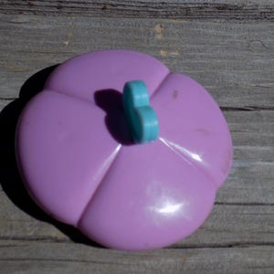 May include: A purple plastic flower with a blue butterfly-shaped button in the center.