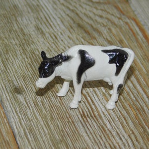 May include: A black and white plastic toy cow figurine. The cow is standing on a wooden surface.