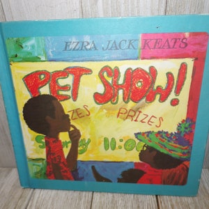 May include: A colorful book cover with the title "Pet Show!" in red letters. The cover features two children, one with a red shirt and the other with a green and blue hat. The book is by Ezra Jack Keats.