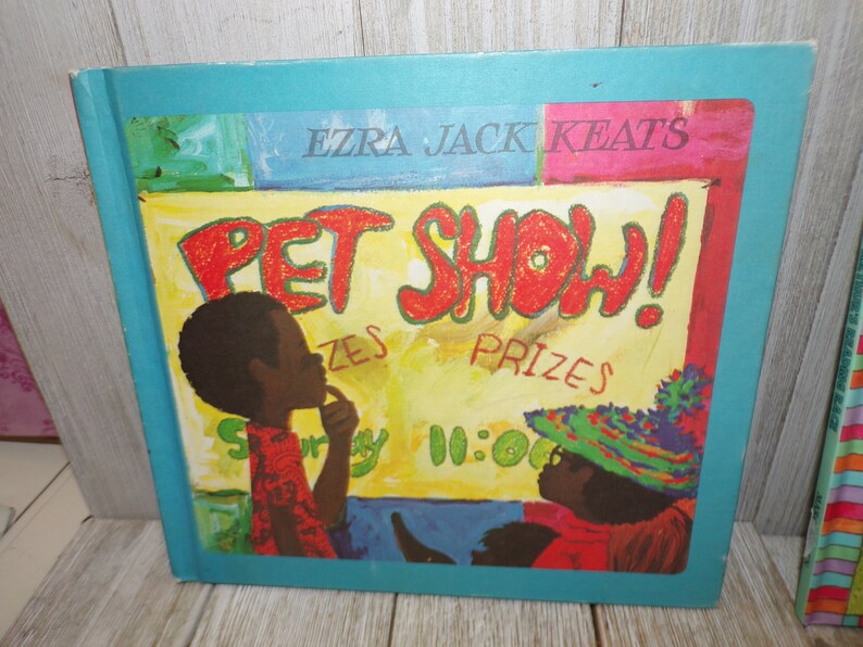 May include: A colorful book cover with the title "Pet Show!" in red letters. The cover features two children, one with a red shirt and the other with a green and blue hat. The book is by Ezra Jack Keats.