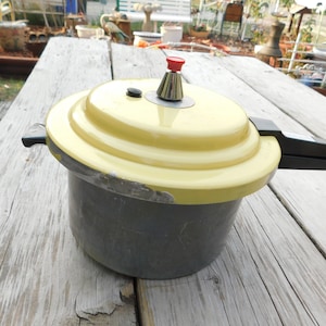 May include: A yellow and gray pressure cooker with a black handle and a red button on the lid.