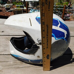 May include: White motorcycle helmet with blue and light blue geometric designs. The helmet is 17 inches tall.  "Do you have it all covered?" is printed on the side of the helmet.