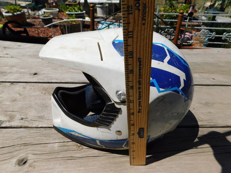 May include: White motorcycle helmet with blue and light blue geometric designs. The helmet is 17 inches tall.  "Do you have it all covered?" is printed on the side of the helmet.