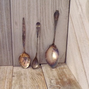 May include: Three vintage silver spoons with ornate handles. The spoons are arranged vertically on a wooden surface.