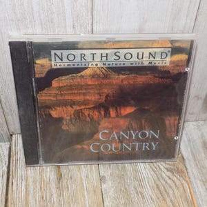 May include: A CD case with the text "NORTH SOUND Harmonizing Nature with Music" and "CANYON COUNTRY". The cover features a landscape image of a canyon with reddish-brown rock formations. The case is in a clear plastic sleeve with a black spine.