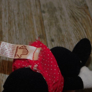 May include: A black and white plush toy wearing a red and white polka dot dress. The toy has a tag that reads "applause." Applause Inc. Woodland Hills. Made in China. The Walt Di. Reg. No. P.A. Contents: All. Item No. 8535.