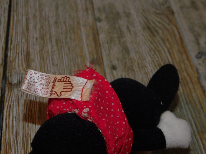 May include: A black and white plush toy wearing a red and white polka dot dress. The toy has a tag that reads "applause." Applause Inc. Woodland Hills. Made in China. The Walt Di. Reg. No. P.A. Contents: All. Item No. 8535.