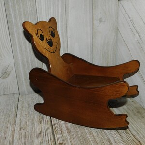 Puede incluir: Una mecedora de madera con forma de oso con la cara pintada. La silla es marr&oacute;n y tiene un dise&ntilde;o sencillo.