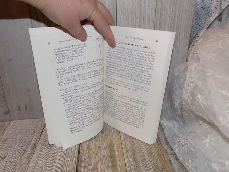 May include: An open book with a white background. The book is open to a page titled "The Old Man's Bundle" and a page titled "Games and Fun with Playing Cards". The text on the page describes the rules for a card game.
