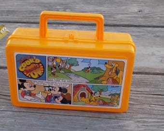 May include: A vintage yellow plastic lunchbox featuring a comic strip with Mickey Mouse, Donald Duck, and Pluto. The lunchbox has a handle and a clasp closure. The comic strip shows scenes from a Disney cartoon.