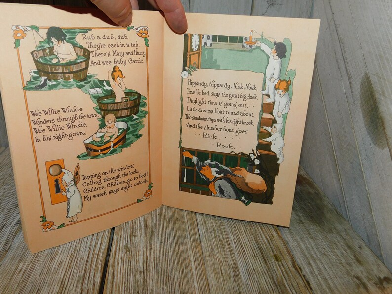 Op de afbeelding: Een open vintage kinderboek met illustraties van kinderen in badkuipen en een klok. De tekst luidt "Rub a dub, dub. They're each in a tub. There's Mary and Harry And wee baby Carrie" en "Hippardy, Neppardy. Nek, Nook, Time for bed, says the great big clock, Daylight time is going out... Little dreams float round about. The panduan taps with his light knock And the slumber boat goes Riek. Rook."