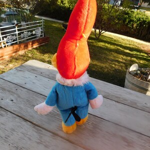 May include: A plush toy of a cartoon character with a red hat, blue overalls, and white gloves. The toy is standing on a wooden surface.