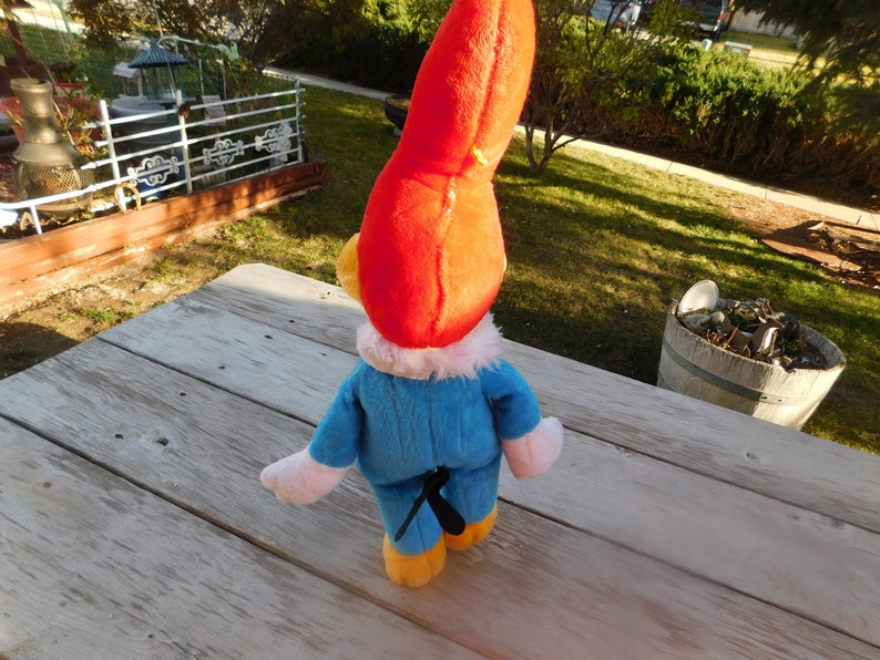 May include: A plush toy of a cartoon character with a red hat, blue overalls, and white gloves. The toy is standing on a wooden surface.