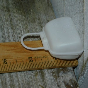Op de afbeelding: Een witte plastic zaagbladbeschermer met een handvat, rustend op een houten liniaal. De afdekking is ongeveer 7,6 cm lang. Op de liniaal staat "MADE IN U.S.A."