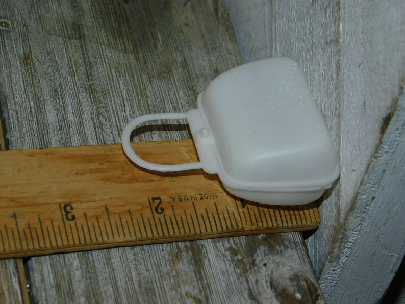 Op de afbeelding: Een witte plastic zaagbladbeschermer met een handvat, rustend op een houten liniaal. De afdekking is ongeveer 7,6 cm lang. Op de liniaal staat "MADE IN U.S.A."