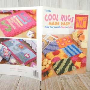 May include: A book titled "Cool Rugs Made Easy" with a pink and blue rug with the word "Smile" on it, a blue and pink rug with flowers, and a multi-colored rug with different patterns.