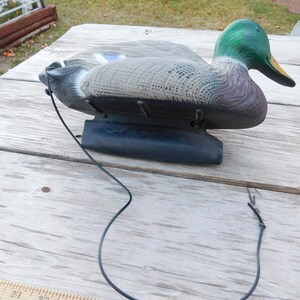 May include: A green-headed mallard duck decoy with a black base and a string attached. The decoy is made of plastic and has a realistic appearance.