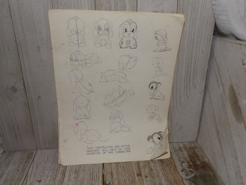 May include: A vintage sheet of paper with pencil sketches of a cartoon dog in various poses. The drawings show construction and action diagrams to help with animation. The paper is aged with visible wear and tear.