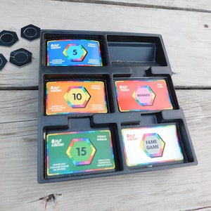 May include: A black plastic game tray with five colorful cards. The cards are for the game "Sale of the Century" and feature numbers 5, 10, 15, the word "Winner", and the phrase "Fame Game".