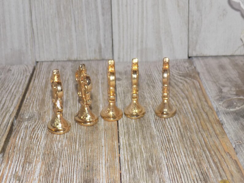 May include: Set of six gold-tone metal decorative place card holders. Each holder features a decorative design with a raised centre.