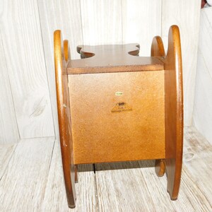 Puede incluir: Una silla mecedora de madera con un peque&ntilde;o estante en la parte posterior. La silla est&aacute; hecha de madera marr&oacute;n claro y tiene un dise&ntilde;o sencillo. El estante tiene una etiqueta que dice "Early American Heritage Woodcraft".